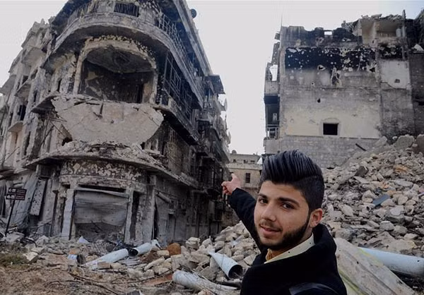 Người đàn ông chỉ tay về phía tòa nhà đã bị tàn phá nặng nề trong cuộc nội chiến Syria.