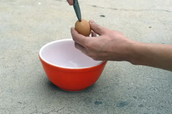 Bước 2: Dùng dao nhọn khoét một lỗ trên quả trứng gà, dùng đầu đũa cho vào trong đảo nhẹ, vừa đảo vừa lắc để ruột trứng ra ngoài, để vỏ trứng qua một bên. 