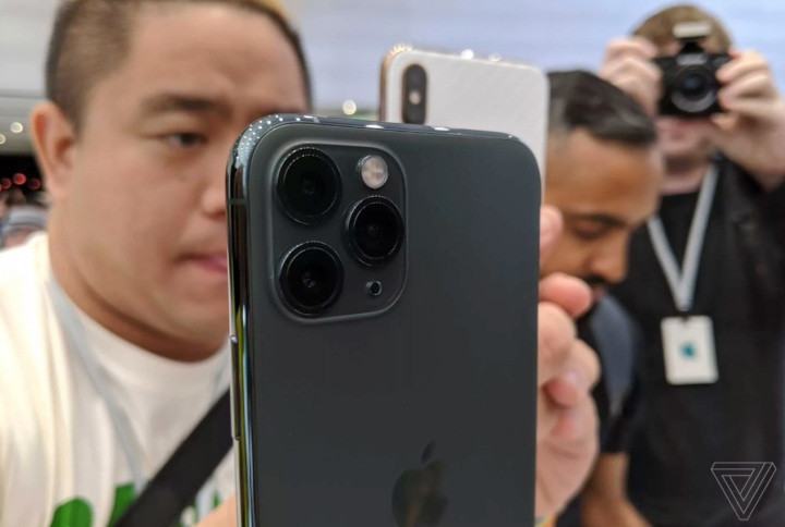 Hãy nói về cụm camera mới này. Đầu tiên là nó khá lớn. Nhưng Apple chẳng thèm giấu đi cụm camera lồi khổng lồ hình vuông này. Nhiều người không thích điều đó, nhưng rồi họ cũng sẽ dùng ốp lưng thôi, nên cũng chẳng có vấn đề gì đáng phàn nàn. Hiển nhiên, Apple rất giỏi trong việc bố trí ánh sáng tại khu vực "trên tay" sản phẩm, nên phóng viên TheVerge không thể đánh giá camera của iPhone 11 Pro/11 Pro Max một cách nghiêm túc. Nhưng khi thử qua giao diện camera mới thì họ nhận thấy nó rất tuyệt. Khi bạn chụp ở chế độ chuẩn, viewfinder sẽ lấp đầy màn hình. Và nếu bạn trượt sang chế độ góc rộng và telephoto (thay vì bấm như trước đây), nó sẽ hiển thị một thanh trượt cho bạn biết mức độ zoom theo hệ số và milimet.