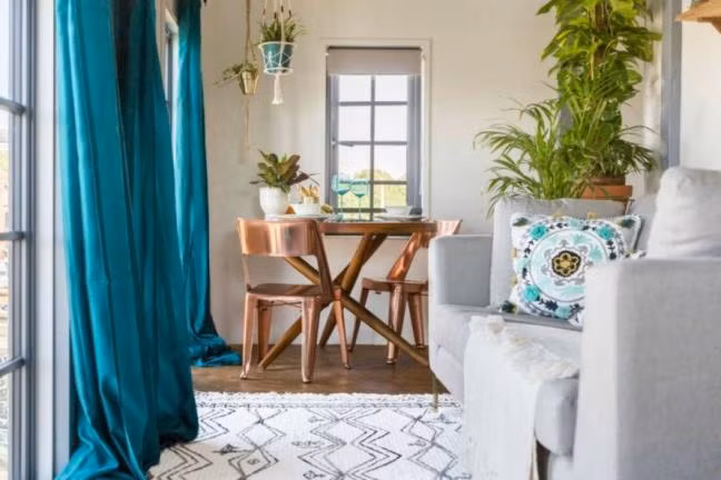 Phòng khách ngôi nhà nổi bật với bộ ghế sofa xám, thảm trắng sọc họa tiết đen, màn cửa màu xanh, tất cả tuy đối lập gam màu nhưng tóm lại, chúng làm nổi bật không gian tổng thể ngôi nhà cần cẩu này.