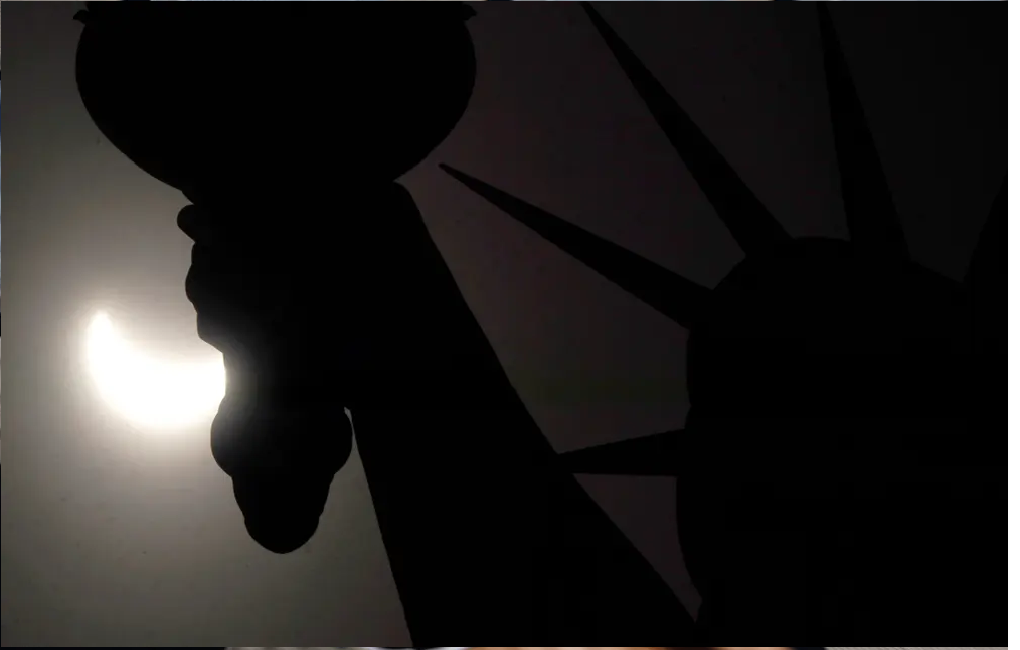 Nhật thực một phần di chuyển trên bầu trời gần vương miện của Tượng Nữ thần Tự do ở New York. Ảnh: Theguardian.