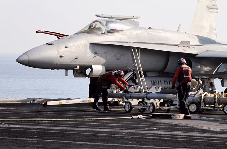 Trong ảnh là kỹ thuật viên hỗ trợ trên boong tàu USS Eisenhower đang tháo vũ khí từ một chiếc F/A-18E/F sau khi nó hạ cánh, số vũ khí này sẽ được chuyển xuống phía dưới khoang chứa vũ khí bên trong thân tàu và sẽ được sử dụng cho đợt xuất kích tiếp theo.