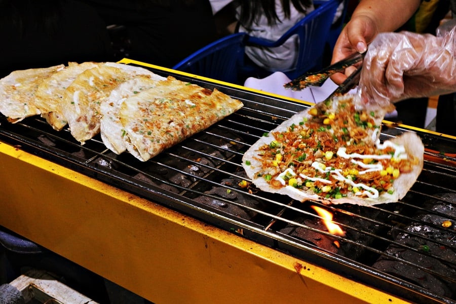  Bánh tráng nướng: Với những du khách đã từng du lịch Đà Lạt, chắc chắn đều một lần thử qua hương vị thơm ngon, giòn rụm của chiếc bánh tráng nướng nóng hổi. Về phần nguyên liệu, bánh được nướng trên bếp than hồng đến khi vừa chín tới thì cho thêm trứng gà (hoặc trứng cút) trộn đều cùng hành lá, xúc xích, ruốc khô, phô mai và tương ớt. Giữa tiết trời se lạnh của Đà Lạt mà được thưởng thức một chiếc bánh tráng nướng thơm phức cũng đủ làm bạn thấy ấm lòng. Ảnh minh họa