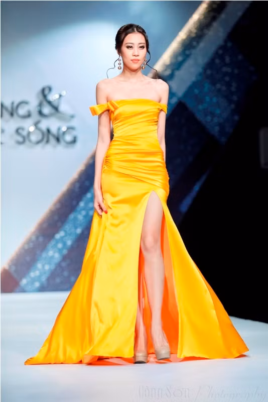 Mẫu thiết kế váy dạ hội màu vàng rực với chi tiết xẻ tà cao giúp Kiki Lê khoe được đôi chân dài, phần vai trễ nải làm tăng thêm vẻ đẹp quyến rũ.