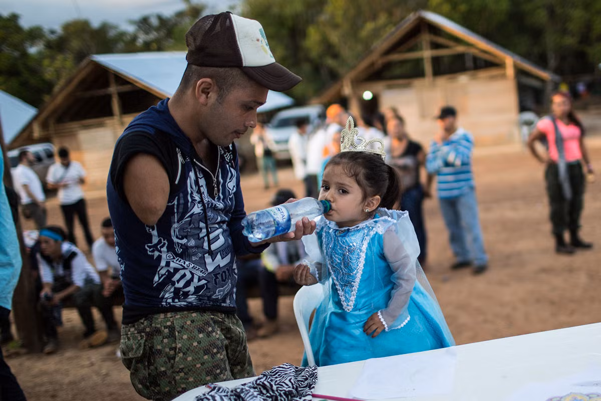 Một thành viên FARC bị cụt tay đang giữ chai nước cho một bé gái tại buổi cầu nguyện. Ảnh AJ