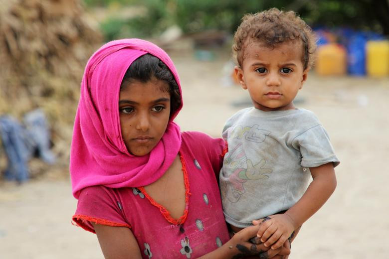 Một bé gái bế em trong khu trại tị nạn gần thành phố Aden, Yemen.