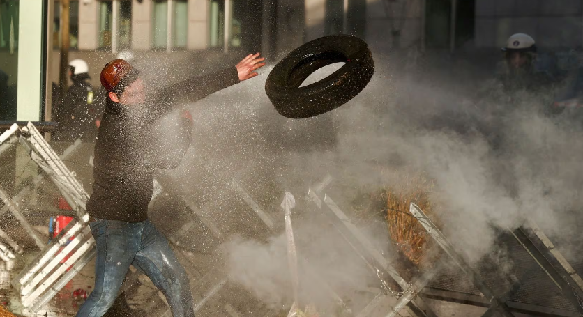 Một người đàn ông ném lốp xe qua hàng rào trong cuộc biểu tình tại Brussels, Bỉ, ngày 1/2.