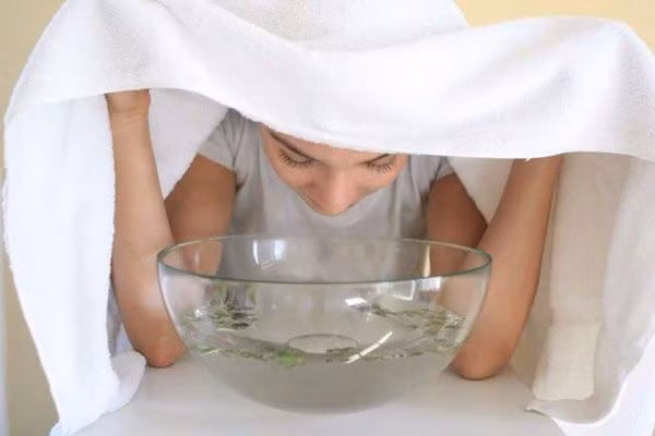 Sau khi đun nước xông, bạn dùng khăn tắm trùm qua đầu trong 10 - 20 phút, thi thoảng dùng đũa khoắng nước để hơi nước tỏa ra đều nhất. Ảnh: anhp.