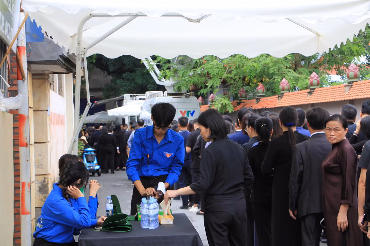 Hàng dài người xếp chờ viếng và được các đoàn viên, thanh niên hỗ trợ nước, khăn giấy.