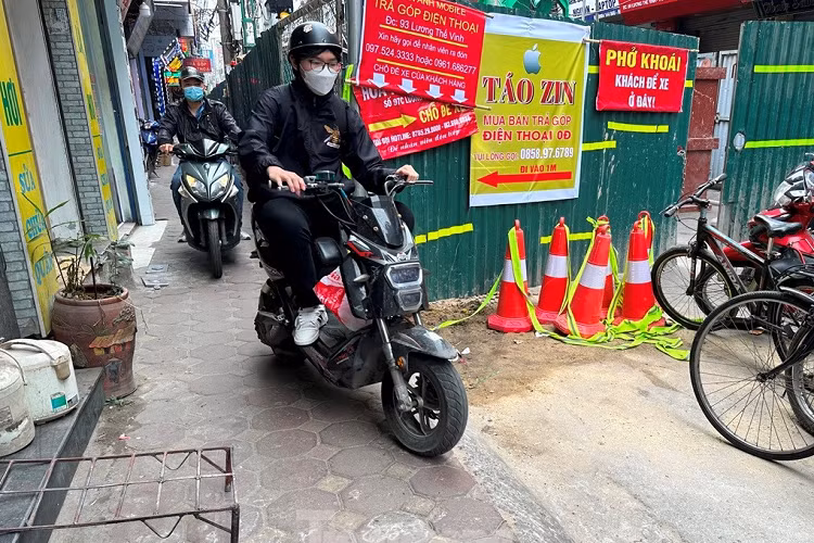 Người dân đi bộ và xe máy luồn hàng rào công trường để đi lại.