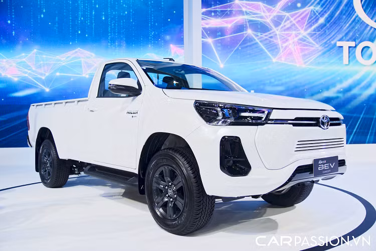 Những thay đổi này có thể nhìn thấy rõ nhất ở phần đầu xe, nơi Toyota đã thiết kế mặt ca-lăng khép kín cho chiếc bán tải thay vì trang bị lưới tản nhiệt. Phần viền bóng đèn LED chính cũng được phủ màu xanh dương, chi tiết đặc trưng của những mẫu xe Toyota có mô-tơ điện.
