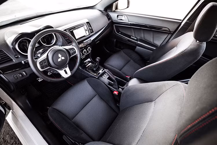 Nội thất bên trong chiếc xe thể thao Mitsubishi Lancer EVO Final Edition này thiết kế đơn giản với tông màu đen làm chủ đạo. Ghế ngồi thể thao chỉnh cơ, bọc da lộn một phần kết hợp những đường chỉ đỏ tương phản.