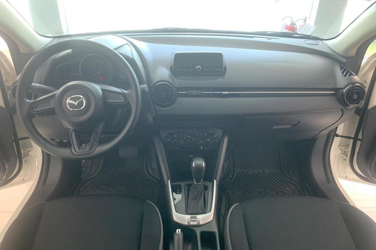 Bên trong xe, Mazda2 Sedan 2023 bản 1.5L AT chỉ có ghế bọc nỉ, ghế trước chỉnh cơ, màn hình analog + kỹ thuật số, hệ thống âm thanh 4 loa, khởi động nút bấm và cửa sổ chỉnh điện bên ghế lái.