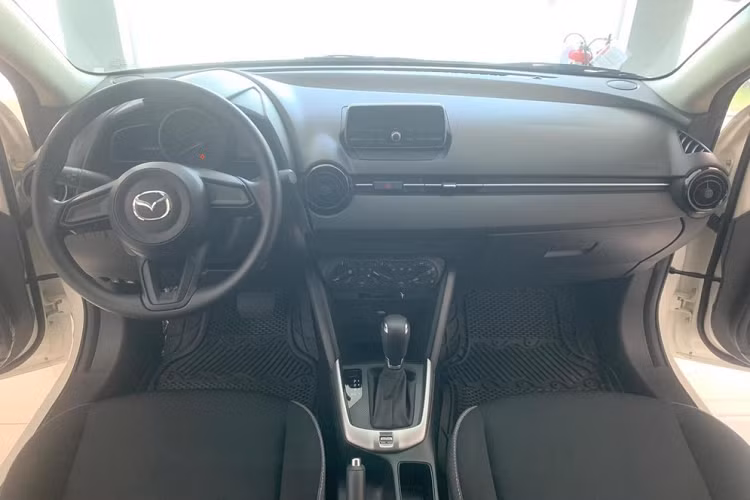 Bên trong xe, Mazda2 Sedan 2023 bản 1.5L AT chỉ có ghế bọc nỉ, ghế trước chỉnh cơ, màn hình analog + kỹ thuật số, hệ thống âm thanh 4 loa, khởi động nút bấm và cửa sổ chỉnh điện bên ghế lái.