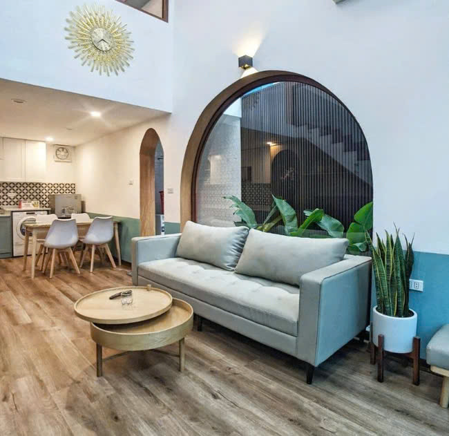 Phần tường kính sau sofa là điểm nhấn dành cho phòng khách, là nơi gia chủ có thể thỏa mãn sở thích trang trí cây cảnh của mình. Ảnh: Nguyễn Nhung Tiếp nối với không gian phòng khách là khu vực bếp, bàn ăn của gia đình. Trước đó, giữa phòng bếp và phòng khách có một bức tường ngăn. Nhóm kiến trúc sư quyết định đập bỏ bức tường này để tạo nên một không gian liền mạch, có chiều sâu cho khu vực sinh hoạt chung. Để phù hợp với diện tích ngôi nhà, nhóm đã thiết kế bếp hình chữ L, không gian vừa đủ để gia chủ có thể thoải mái nấu nướng mỗi ngày. Hệ tủ bếp màu trắng - xanh được phối hợp với gạch bông bắt mắt.