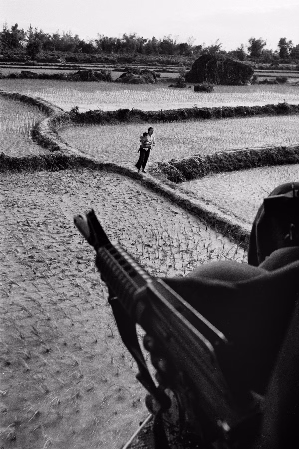 Người phụ nữ Việt bế con đứng trên bờ ruộng, nhìn từ một xe thiết giáp Mỹ. Ảnh: Catherine Leroy.