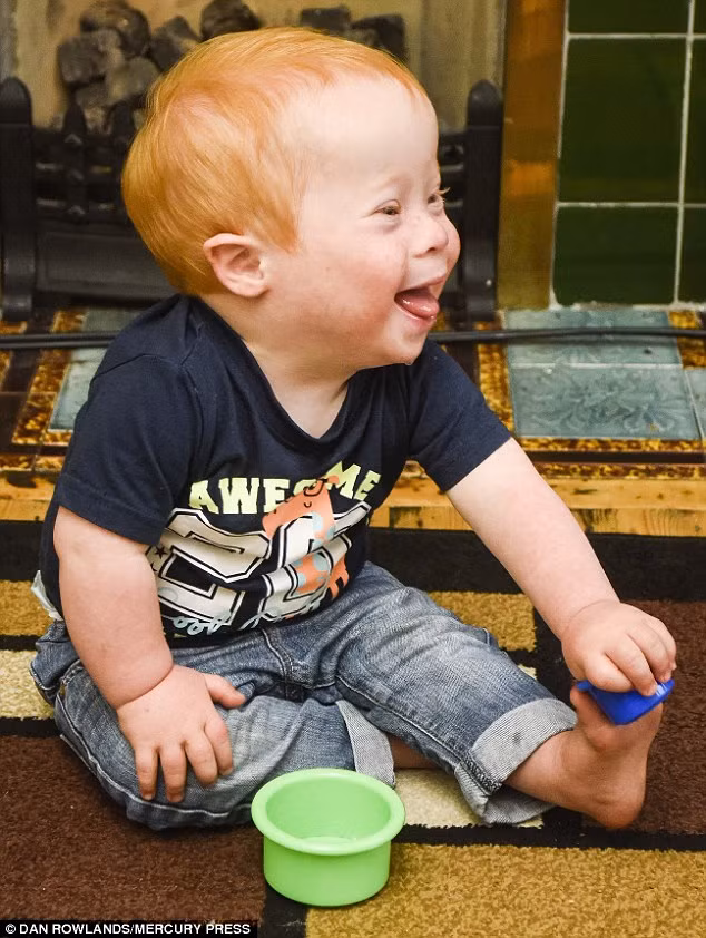 Cậu bé cười khúc khích khi ngồi bên lò sưởi với đồ chơi của mình.