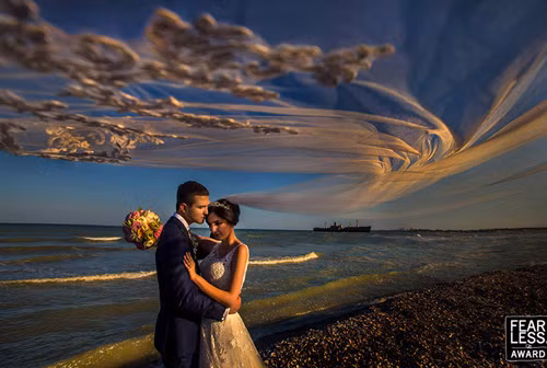 Dải voan như những đám mây mong manh trên nền bầu trời về tối kết hợp hoàn hảo với bờ cát sỏi sẫm màu và hình con tàu xa xa để làm nổi bật hai nhân vật chính.