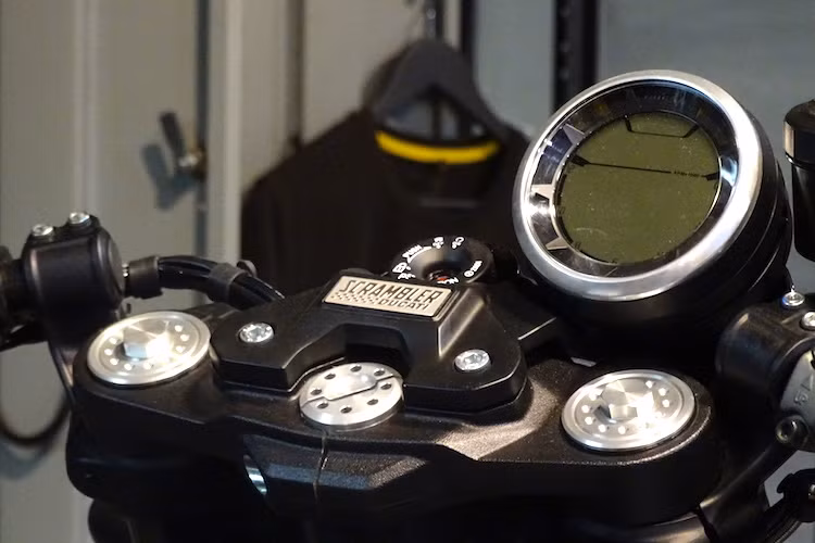 Để che đi lỗ bắt gù ghi-đông trên chảng ba, Ducati đã sử dụng một tấm thép với bảng tên Scrambler khá đẹp mắt. Đồng hồ điện tử tròn của xe hoàn toàn không có thay đổi so với các bản Scrambler khác.