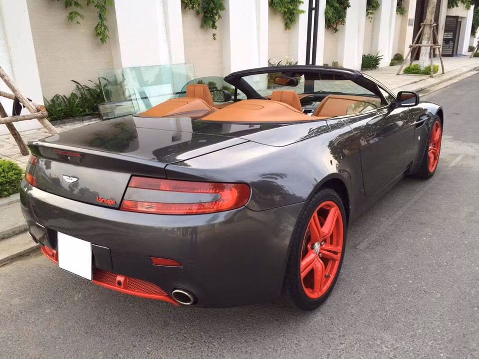 Chiếc V8 Vantage Roadster này được nhập vào Việt Nam từ năm 2009 với màu xám nòng súng khá giống như những chiếc Aston Martin của Điệp viên 007 James Bond. Để tạo điểm nhấn cho chiếc xe, chủ nhân của nó cũng đã sơn màu đỏ mờ ở mâm cùng phần dưới cản sau.