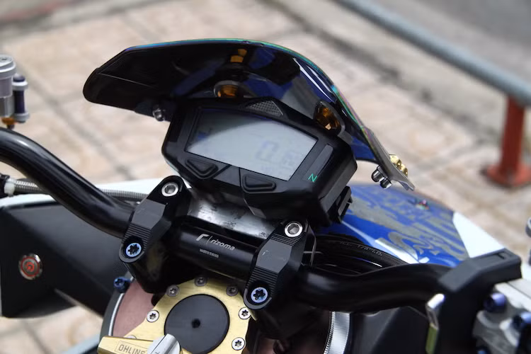 Cụm ghi-đông kèm gù được chủ xe lựa chọn vốn dành cho mẫu naked bike PKL Ducati Monster, nhưng đã được chế vào Click một cách khéo léo nhờ có thớt cổ được "thửa riêng". Ở phía trên ghi-đông là đồng hồ điện tử Koso DB-03 được che bởi kính chắn gió tự chế với lớp phủ 7 màu.