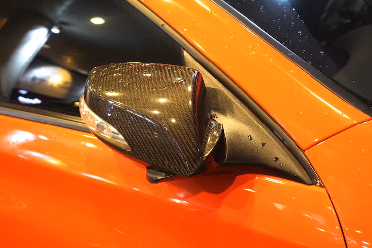 Nổi bật trên nền sơn cam của xe, chủ nhân đã tạo điểm nhấn với ốp gương bằng sợi carbon và mui xe được sơn đen, cùng với những đường kẻ họa tiết trang trí màu cam chạy dọc từ nắp ca-pô lên.