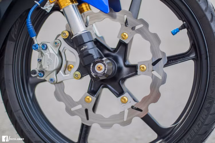 Bắt đầu từ phía trước, chiếc xe đã được nâng cấp với cặp phuộc kiểu dáng khỏe khoắn hơn của hãng 7Speed. Trong khi đó, "dàn chân" nguyên bản của Exciter đã được thay bằng cặp mâm 6 cánh xoắn của Honda CBR150 đầy khỏe khoắn, đồng thời hệ thống phanh trước đã được nâng cấp với đĩa Galfer và heo Brembo 2 pis đối xứng.