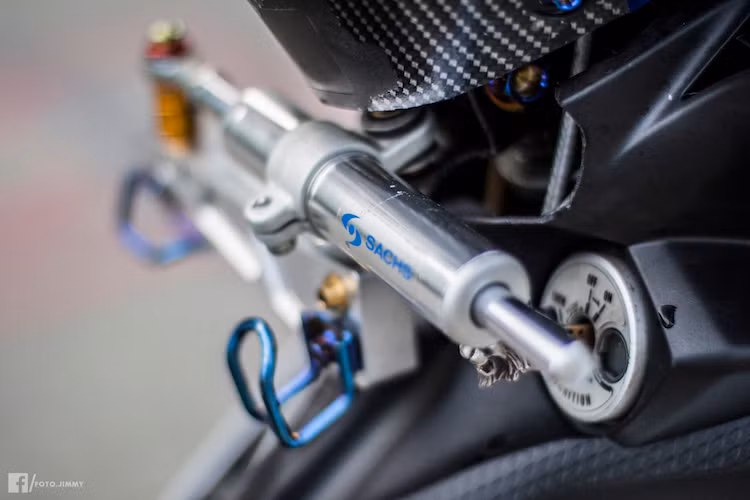 Trong khi đó, ở bên dưới cổ xe, nhựa ốp lườn cũng đã được cắt gọn, tạo không gian gắn thêm cây trợ lực Sachs lấy từ xe Aprilia, khiến cho Exciter 135 độ trở nên ổn định hơn khi chạy ở tốc độ cao.