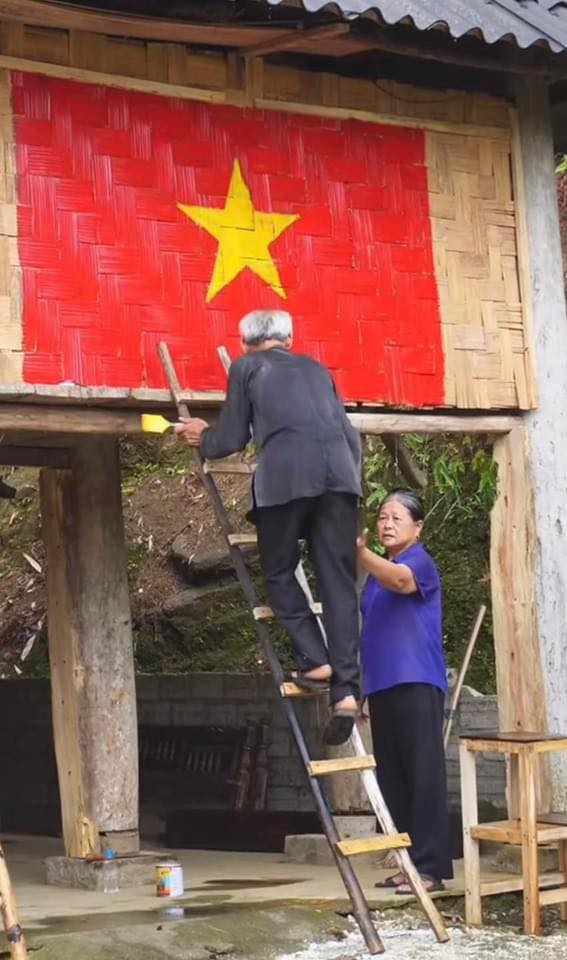 Cụ ông trèo lên chiếc thang tự làm, cụ bà ở dưới vừa giữ thang, vừa lấy lọ sơn màu cho ông.