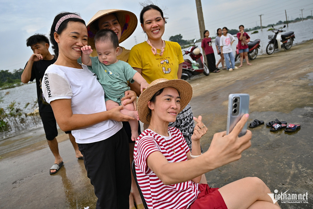 Chị Nguyễn Thị Hiền (40 tuổi, Quốc Oai) hào hứng giơ máy, tạo dáng chụp ảnh cùng hội chị em trong xóm. "Nhà gần đây nên cả tuần nay chiều nào mấy chị em cũng đưa các con ra đây nghịch nước, vui chơi cho mát. Phía trước cánh đồng đang bị ngập rất rộng, lại có dòng chảy đi qua nên không lo nước ứ đọng hoặc có rác trôi nổi", chị Hiền nói.