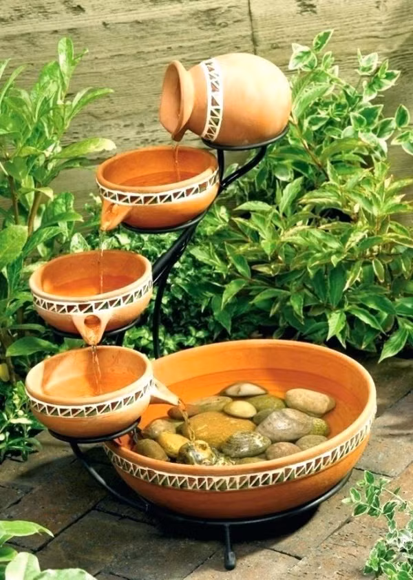 Chọn một chiếc kệ nhỏ xinh xinh, chọn thêm những chiếc bát gốm có vòi rót nước, vài viên đá cuội ở bát cuối cùng là đủ để có thác nước mini tuyệt đẹp cho góc sân nhỏ. Màu sắc của chất liệu gốm sẽ giúp không gian dịu dàng và gần gũi trong những ngày hè.