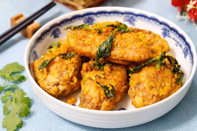 Gắp cánh gà sốt trứng muối bày ra đĩa và thưởng thức ngay lúc còn nóng, miếng cánh gà thơm bùi hương vị của trứng muối, vỏ ngoài giòn giòn đậm đà ngon khó cưỡng.