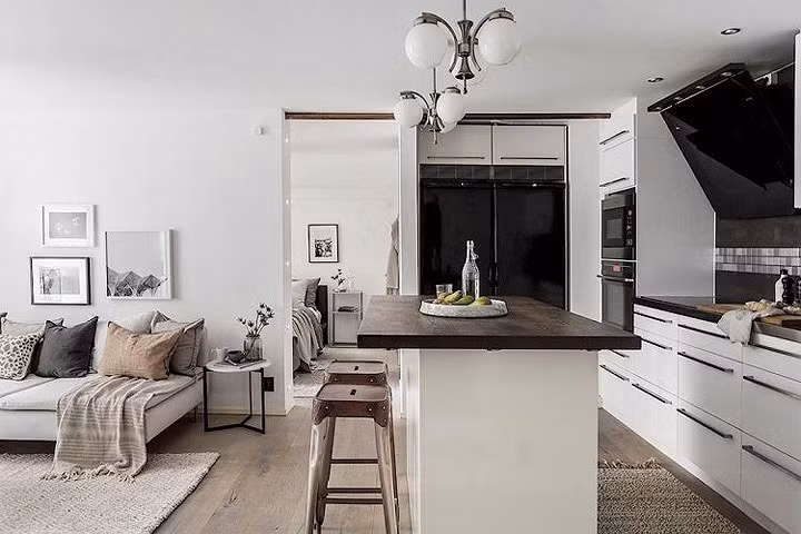 Do diện tích nhà hạn chế, không gian nhà bếp được bố trí gần phòng khách, ngăn cách bởi bar. Gia chủ lắp đặt tủ bếp trắng, thiết bị nấu nướng và bàn ăn dùng tông màu tối.