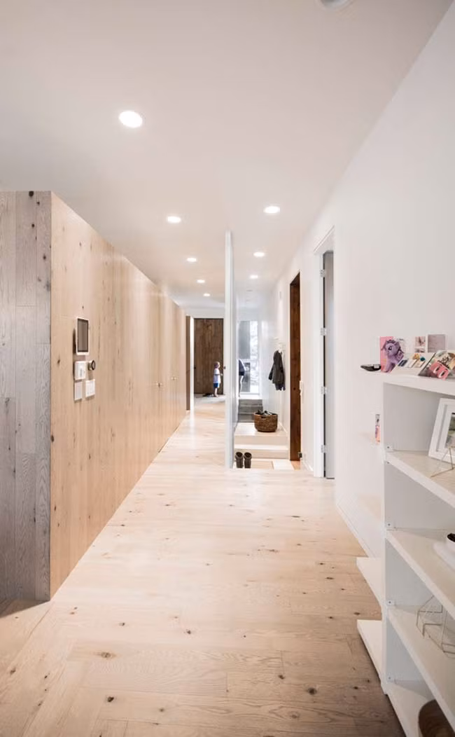 Cánh cửa phòng ngủ được ngăn cách với không gian sống bằng một tấm chắn cây gỗ thích màu trắng giúp kéo dài dạng hình của các cột bên ngoài qua ngôi nhà.