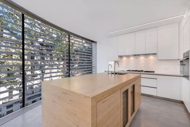 Nhà bếp có một đảo bếp ở giữa, xung quanh là tủ bếp màu trắng.