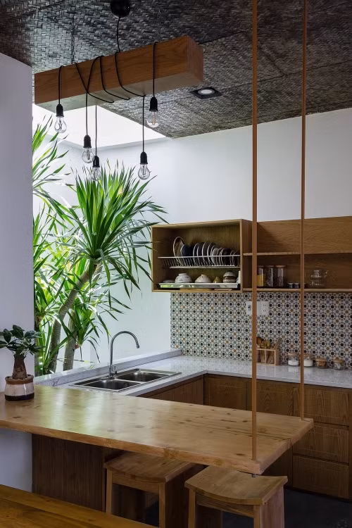 Tủ bếp không cánh cùng lá cọ xanh mang lại cảm giác khoáng đạt. Các vật dụng trong bếp cũng được chủ nhân tinh tế chọn lựa sao cho đồng bộ với cả căn nhà.