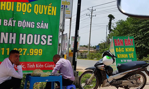 Nhân viên tiếp thị đất dựng pa nô, che dù ngoài vỉa hè để rao bán đất.