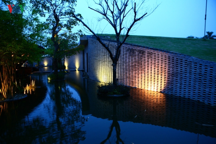 Bên cạnh lối vào là nhà phụ trợ được xây bằng đá và mái phủ cỏ. Điểm xuyết trên mặt nước là những cây xanh.