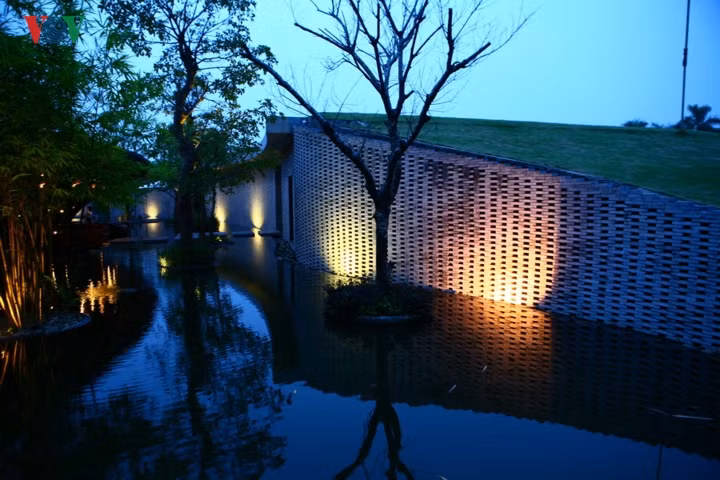 Bên cạnh lối vào là nhà phụ trợ được xây bằng đá và mái phủ cỏ. Điểm xuyết trên mặt nước là những cây xanh.