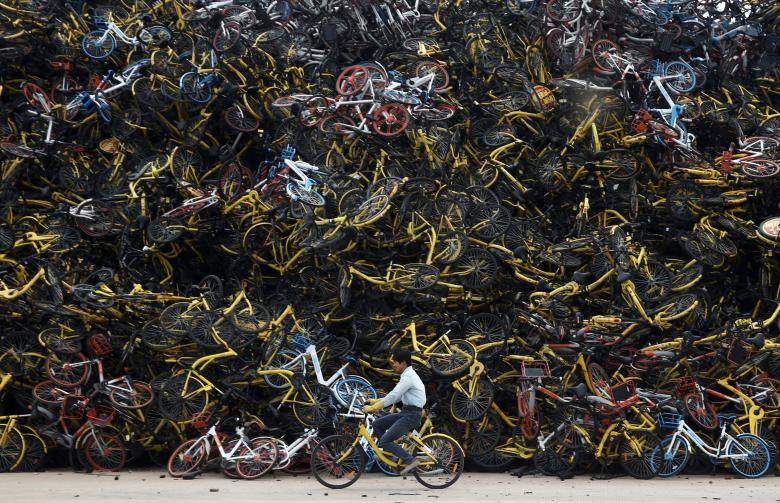 Công nhân đi xe đạp qua đống xe chất đầy tại Hạ Môn, tỉnh Phúc Kiến.
