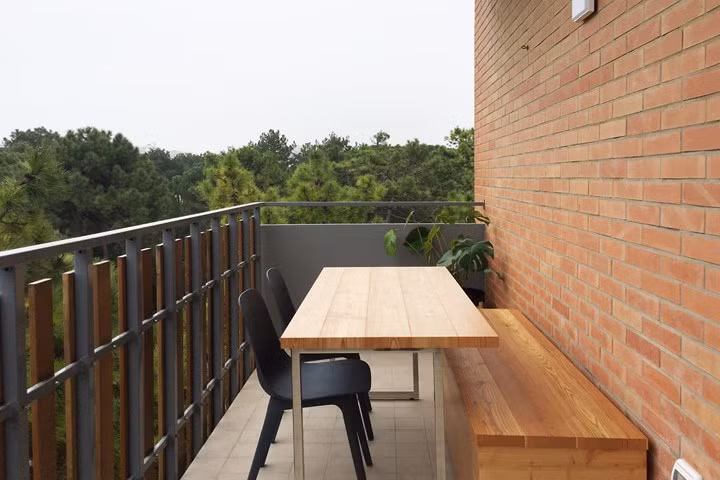 Góc ban công nhỏ là nơi chủ nhân có thể yên tĩnh ngồi đọc sách và gặp gỡ bạn bè, bức tường gạch thô mộc cùng bộ bàn ghế gỗ tạo thế cân bằng cho không gian.