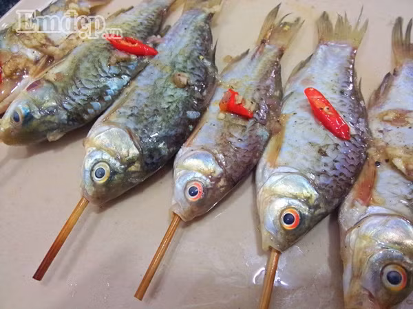 Bước 4: Cho một chút nước cốt chanh vào cá rồi xiên cá vào que xiên, xiên từ miệng cho đến đuôi cá, bằng cách này khi nướng cá sẽ không bị cong.