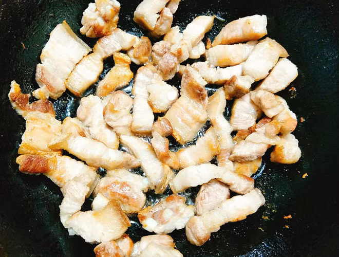 Bước 4: Đặt chảo lên bếp rồi cho thịt ba chỉ vào xào để thịt ra bớt mỡ, đảo đều và xào cho thịt chuyển màu xém vàng mới cho gừng, tỏi, ớt, hành lá vào xào cùng cho thơm mới cho dưa muối mặn vào đảo đều.