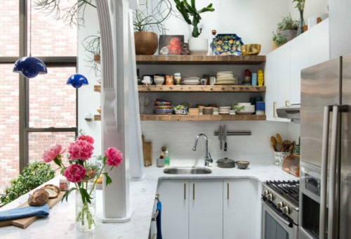 Ngoài việc lắp đặt cửa sổ kính để mang thật nhiều ánh sáng tự nhiên vào nhà, căn bếp còn được sơn toàn bộ với màu trắng tinh khôi. Tủ bếp chọn màu trắng cùng tông với màu nền, vừa giúp bếp gọn gàng vừa tăng thêm không gian lưu trữ. Vì bếp nhỏ, chủ nhân của nó chỉ lắp đặt hệ thống tủ phía dưới bàn chuẩn bị đồ ăn và một phần của bức tường. Góc tường còn lại được bố trí lắp đặt kệ gỗ, gam màu thân quen, gần gũi nhưng cũng không kém phần quyến rũ, ngọt ngào.