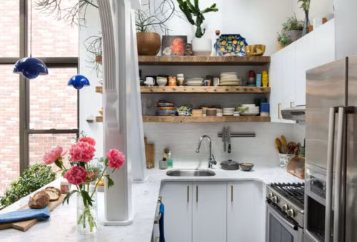 Ngoài việc lắp đặt cửa sổ kính để mang thật nhiều ánh sáng tự nhiên vào nhà, căn bếp còn được sơn toàn bộ với màu trắng tinh khôi. Tủ bếp chọn màu trắng cùng tông với màu nền, vừa giúp bếp gọn gàng vừa tăng thêm không gian lưu trữ. Vì bếp nhỏ, chủ nhân của nó chỉ lắp đặt hệ thống tủ phía dưới bàn chuẩn bị đồ ăn và một phần của bức tường. Góc tường còn lại được bố trí lắp đặt kệ gỗ, gam màu thân quen, gần gũi nhưng cũng không kém phần quyến rũ, ngọt ngào.