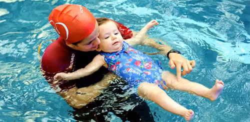 Trong bể bơi, hãy bế bé từ sau lưng, đồng thời nâng nách bé lên, cho bé đập tay đạp chân thỏa thích. Nếu muốn dạy bé cách ngưng thở khi ở dưới nước, hãy bắt đầu bằng việc để một người khác bế lấy bé, cha mẹ ở bên đối diện, thổi phù vào mặt bé để con nhắm mắt, nín thở rồi nhẹ nhàng đưa con hơi chìm xuống nước. Ảnh: songkhoe24