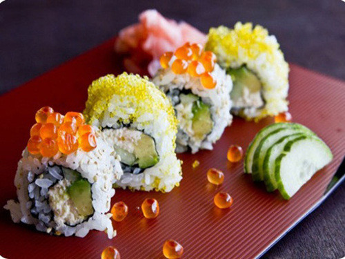 Đặt tấm rong biển lên tấm tre có bọc ni lông và cho cơm vào, dàn đều, mỏng. Rắc hạt vừng lên trên. Lật tấm rong biển vừa làm xuống, rồi xếp bơ, thịt cua, dưa chuột vào một góc. Kế đến dùng tấm tre cuộn tròn sushi cho thật chắc. Lấy cuộn cơm ra khỏi chiếu, rồi cắt làm đôi, sau đó cắt mỗi nửa thành 3 miếng. Ảnh: webphunu