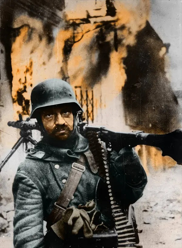 Một binh sĩ Đức quốc xã vác súng máy trên vai và phía sau là một tòa nhà đang bốc cháy. Quân Đức đã thiêu rụi một số làng mạc khi rút khỏi Liên Xô năm 1944.