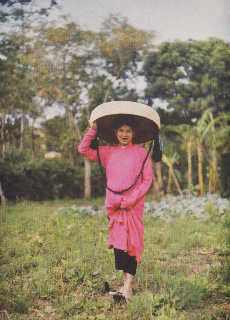 Người phụ nữ trung niên trong trang phục ngày hội với áo dài hồng và nón quai thao. Ảnh: Léon Busy.