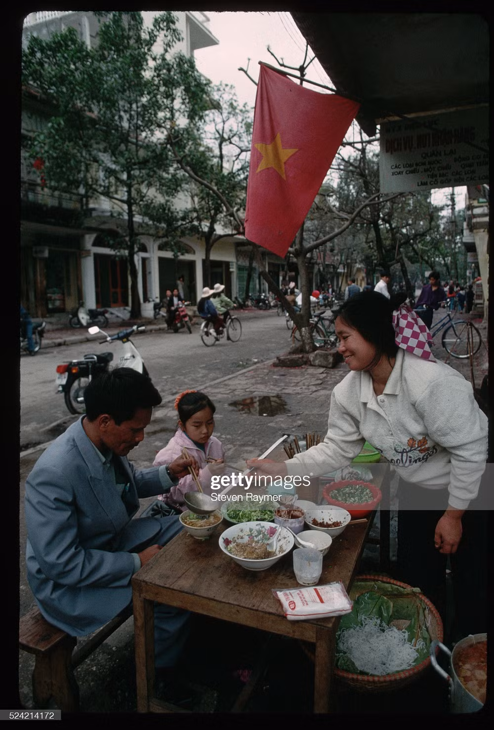 Trong ảnh, hai bố con đang đi ăn một quán bún vỉa hè tại Hà Nội ngày mùng 3 Tết năm 1994. Những ngày này, tìm được quán mở vào Tết không phải chuyện dễ dàng. Ảnh: Steven Raymer.